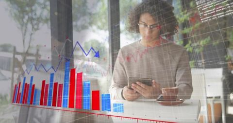 Young man using tablet analyzing stock charts at cafe window with coffee and graphs