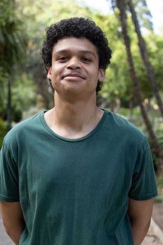 Young man standing and smiling in sunlit park wearing forest green shirt and hoop earring
