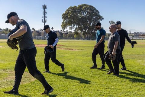 Adult recreational baseball team walking across sunlit field carrying helmets and gloves