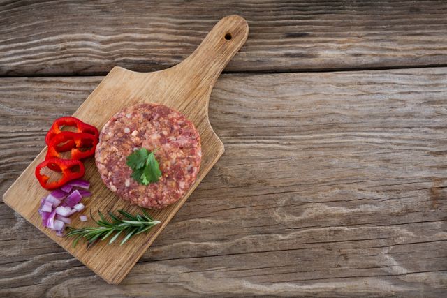Raw beef patty and ingredients on wooden tray against wooden background