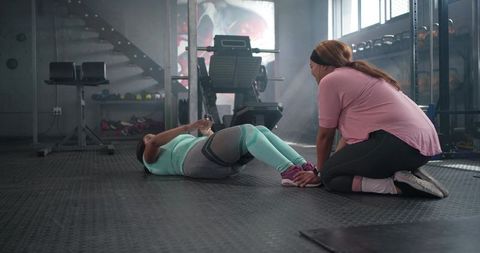 Diverse female training partners doing crunches together in modern gym coaching session
