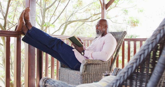 Senior african american man on balcony in log cabin reading book. Log cabin and lifestyle concept.