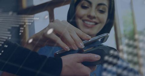 Smiling hispanic woman wearing headscarf using mobile contactless payment at cafe pos