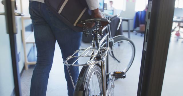 Captures a person bringing their bicycle into an office, promoting an eco-friendly and sustainable commute. Useful for articles or advertisements focused on sustainable living, work-life balance, healthy lifestyles, eco-friendly commuting options, corporate wellness programs, or work environments supportive of alternative transportation.