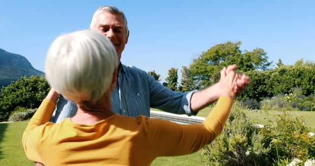 A senior Caucasian couple is joyfully dancing in a sunny garden, with copy space. Their cheerful expressions and active engagement suggest a moment of leisure and happiness in retirement.