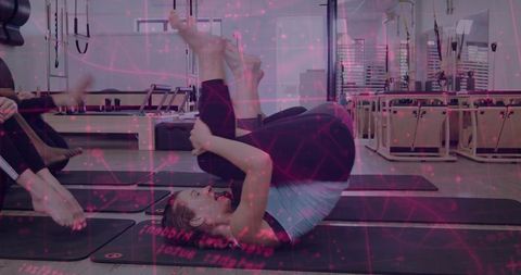 Woman performing Pilates spinal roll on mat in reformer studio with mirrors and equipment