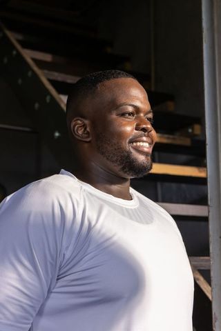 Confident african man standing on industrial staircase smiling in white shirt sunlit loft portrait