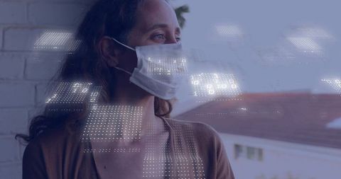 Mid-adult woman wearing face mask gazing through window with dotted digital overlay