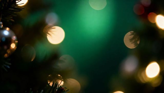 Glistening silver christmas ornament reflecting warm bokeh lights on fir branch