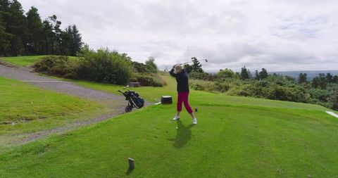 Senior woman swinging golf club on golf course tee box