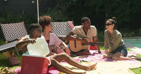 Friends enjoying sunny day with guitar by poolside