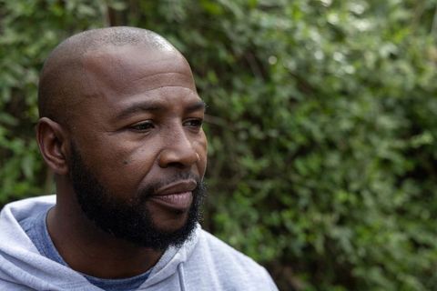 Thoughtful african american man wearing grey hoodie and nose ring outdoors in garden