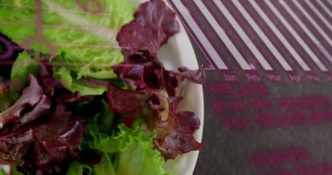 Showing fresh mixed lettuce in white bowl on calendar placemat closeup with vibrant texture