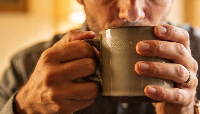 Middle-aged man holding ceramic mug, savoring warm drink in intimate cozy morning close-up
