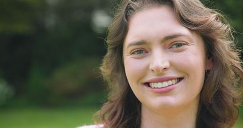 Smiling Woman Posing Outdoors with Green Foliage Background