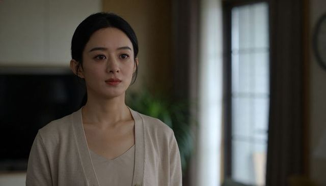 Contemplative asian woman standing in sunlit modern living room wearing beige cardigan, portrait