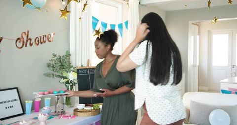 Women arranging pastel cupcakes at indoor baby shower with gender reveal decor
