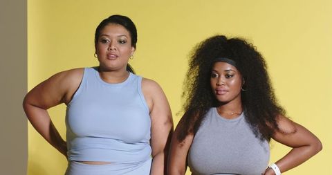 Diverse curvy women wearing athleisure crop tops posing on yellow backdrop with hoops