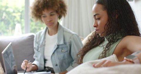 African american friends studying on sofa with laptop and notebook for home learning