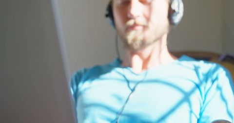 Blurry young man with headphones using laptop in sunny room
