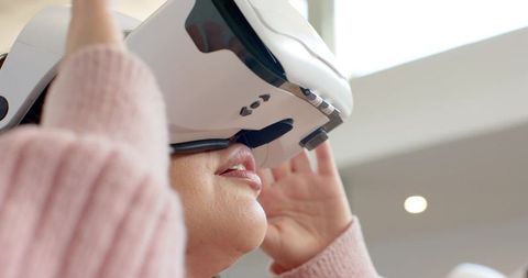 Woman adjusting white vr headset while experiencing virtual reality in modern interior