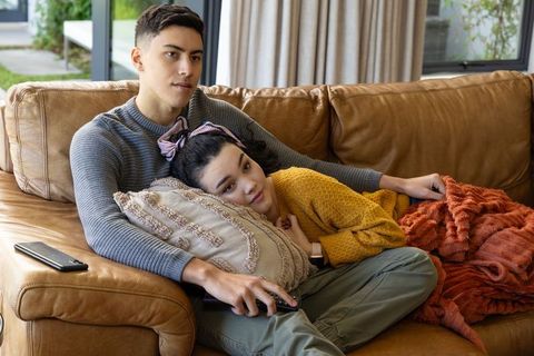Young couple cuddling on leather sofa, woman reclining on pillow while man holding remote