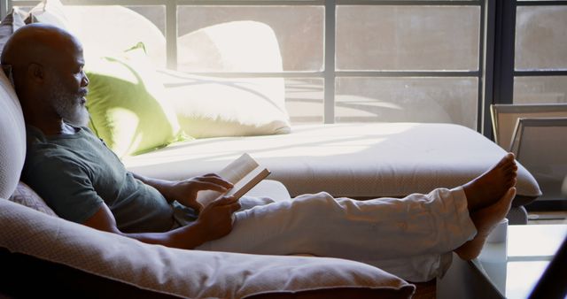 Mature Man Relaxing on Sofa Reading a Book by Window Light - Download Free Stock Images Pikwizard.com