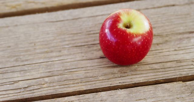 A ripe red apple rests on a wooden surface, with copy space. Its vibrant color contrasts with the rustic texture of the wood, emphasizing freshness and natural simplicity.