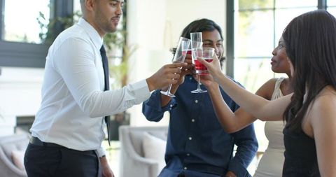 Diverse young adults toasting with red wine glasses in modern bright living room gathering