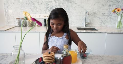 Girl enjoying pancake breakfast with fresh berries in modern kitchen