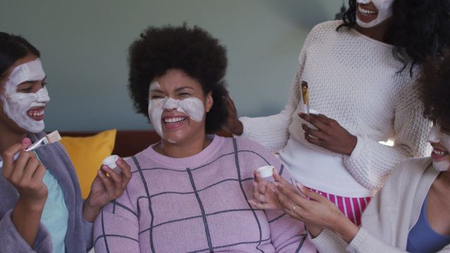 Women of different backgrounds excitedly applying face masks in a cozy indoor setting. The group is clearly enjoying the process, highlighting the themes of togetherness and positive energy around skincare routines. Ideal for campaigns related to beauty products, self-care awareness, and emphasizing communal bonding moments among women.