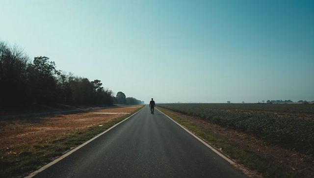 Solitary man walking down empty country road toward distant horizon