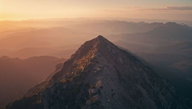 Hikers climbing narrow alpine ridge at golden hour with panoramic mountain vista, warm glow