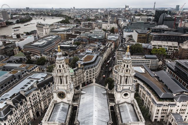 Panoramic aerial view capturing the grandeur of St. Paul's Cathedral prominently in the foreground, surrounded by the sprawling cityscape of London. Ideal for uses in travel brochures, city guides, and articles discussing London architecture, tourism, or historic sites.