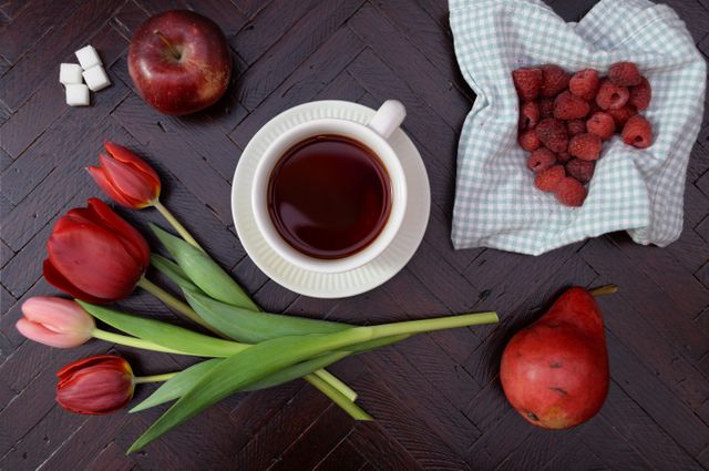 Flat Lay of Tulips, Tea, and Red Fruits on Dark Wood Table - Download Free Stock Photos Pikwizard.com