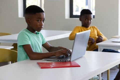 African american schoolboys typing on laptop in classroom focusing on digital learning