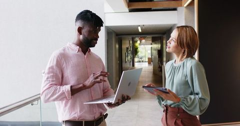 Colleagues Collaborating in Office Hallway with Laptop and Tablet