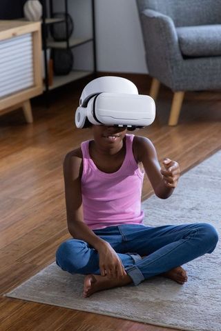 African american girl wearing vr headset sitting on rug reaching, exploring virtual world
