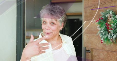 Mature woman greeting at holiday doorway with surprised smile and festive wreath