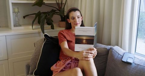 Woman Relaxing on Sofa Reading Paperback Book by Sunlit Window