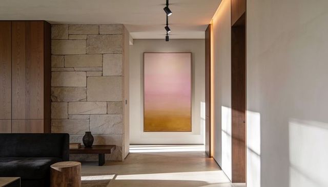Minimalist hallway with tall gradient painting, warm sunlight, stone wall and modern sofa