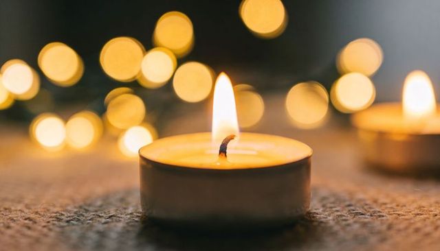 Warm tealight candle glowing on textured surface with bokeh lights creating cozy ambiance