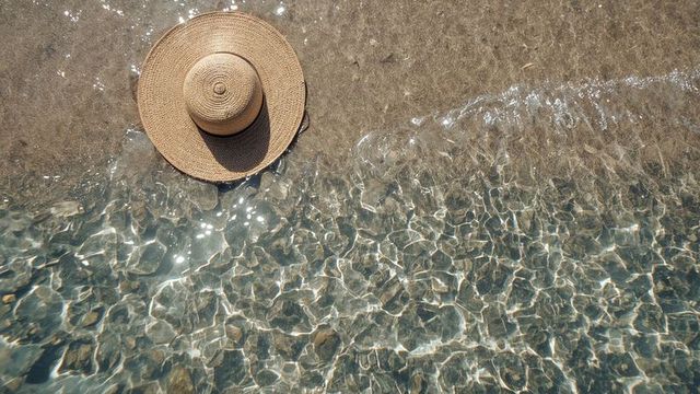 Sun Hat Resting on Clear Beach Water with Sparkling Sunlight