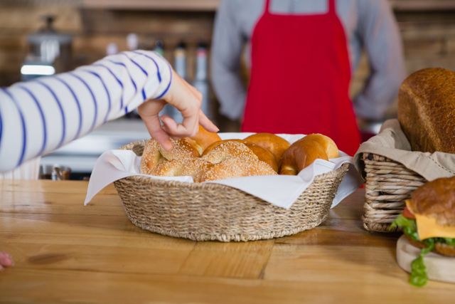 Customer pointing at fresh buns in a basket at a bakery counter. Ideal for use in advertisements for bakeries, cafes, or food-related businesses. Can also be used in articles or blogs about fresh baked goods, customer service, or retail environments.