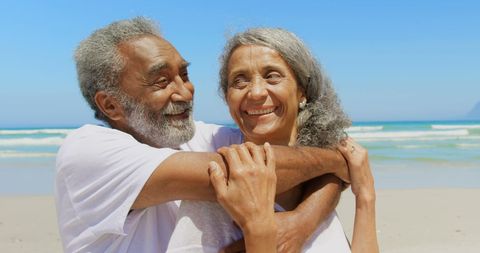 Senior couple embracing joyfully on sunlit beachfront