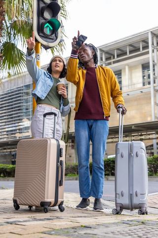 Asian woman and african american man pointing at green arrow while traveling with luggage