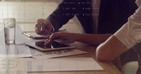 Business colleagues reviewing analytics on tablet and printed charts in boardroom meeting