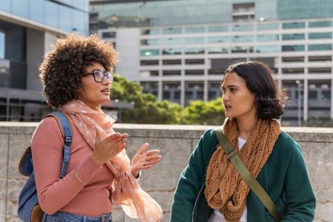 Diverse young women having animated conversation in modern urban plaza near city architecture