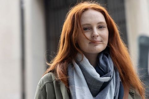 Redhead woman standing on urban street wearing olive jacket and gray-blue scarf closeup