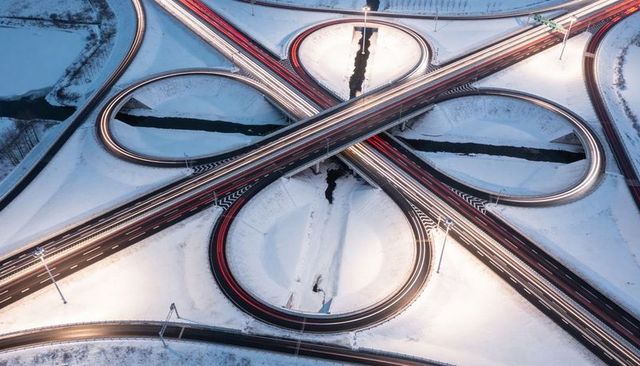 Aerial winter highway interchange forming cloverleaf loops with glowing light trails